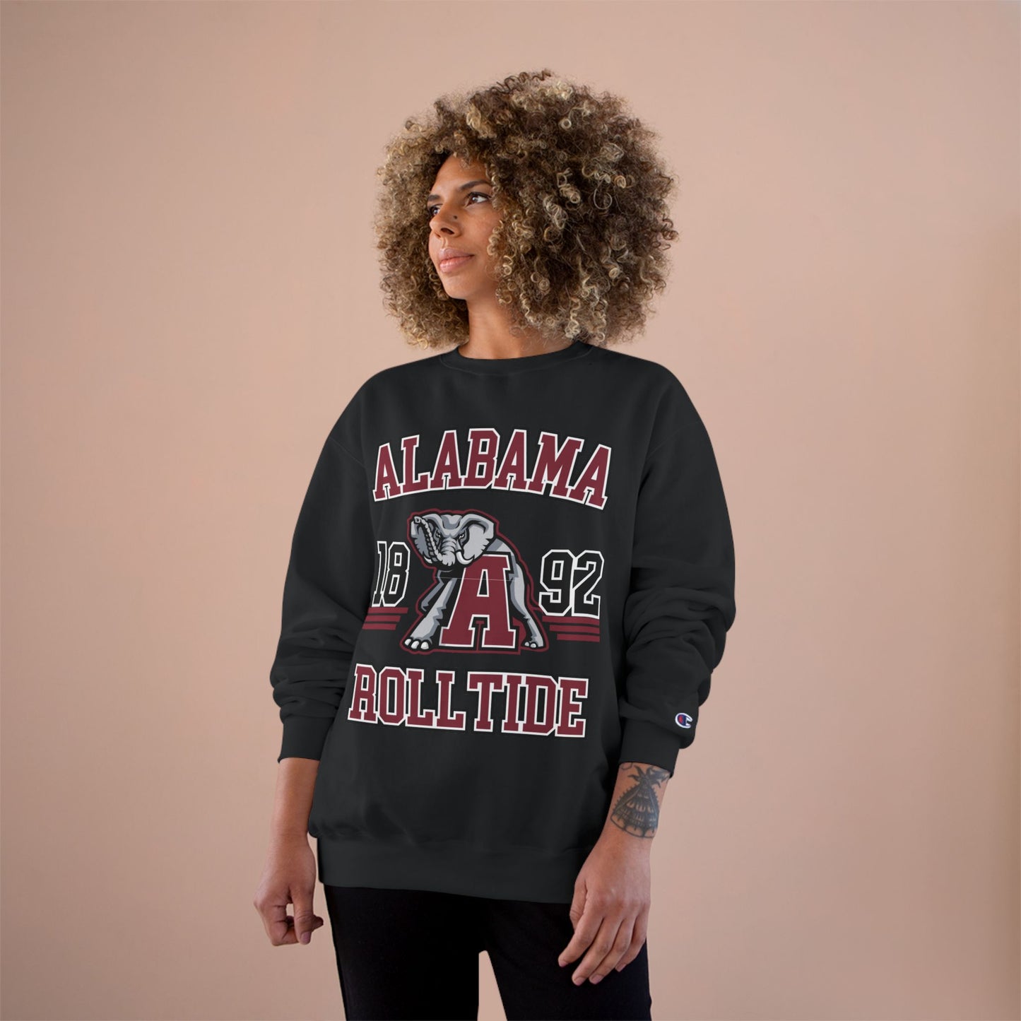 Person wearing a black 'Alabama Roll Tide' sweatshirt with a logo on a beige background