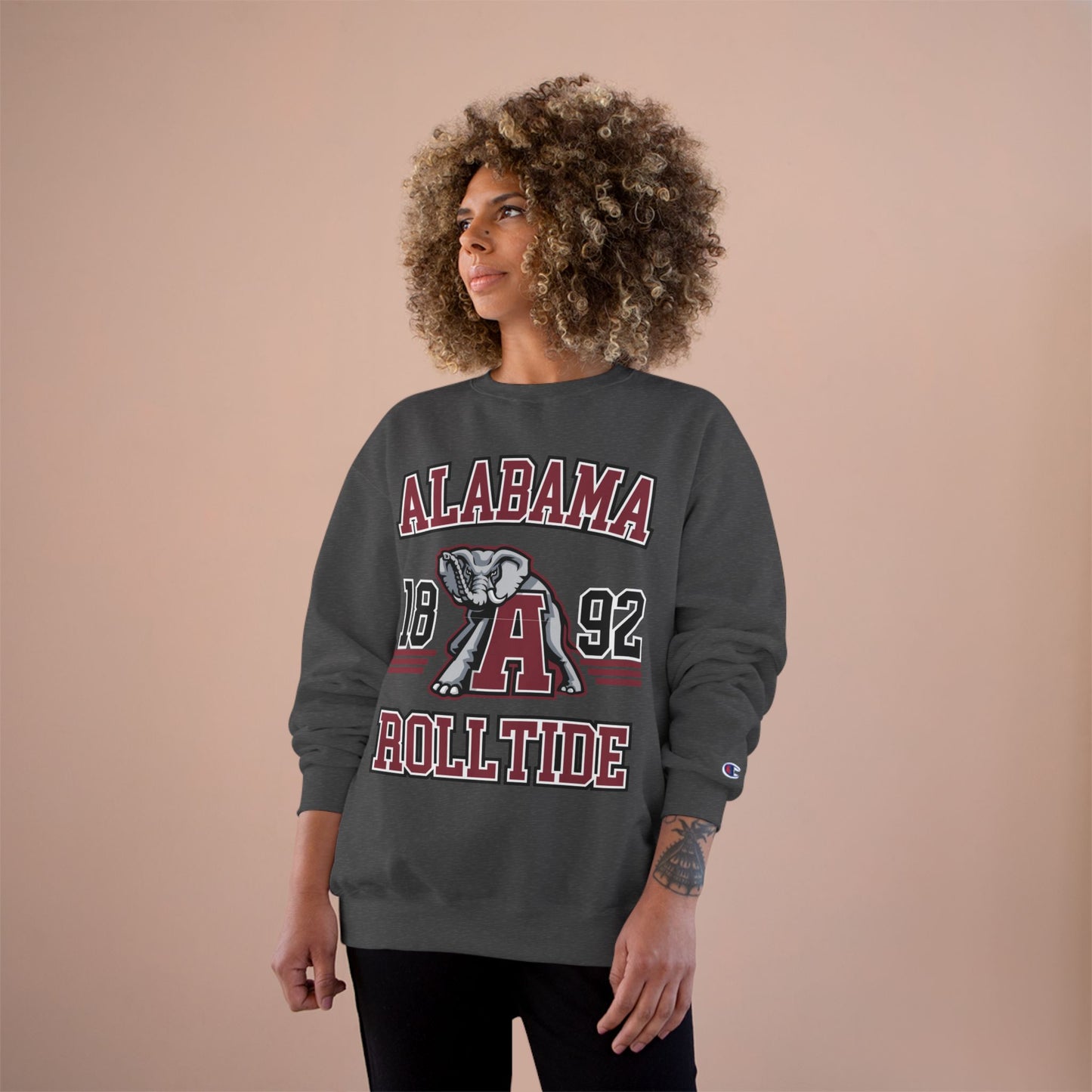 Person wearing a gray 'Alabama Roll Tide' sweatshirt with a logo on a beige background