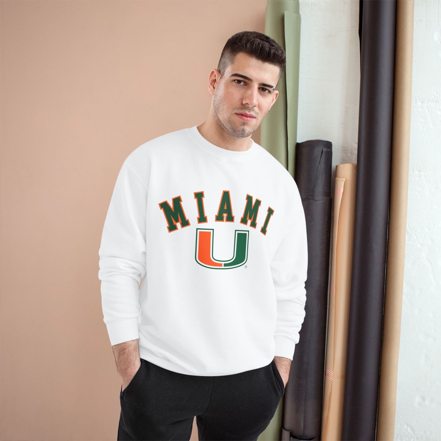 Man wearing a white sweatshirt with 'MIAMI U' print, standing against a beige wall.