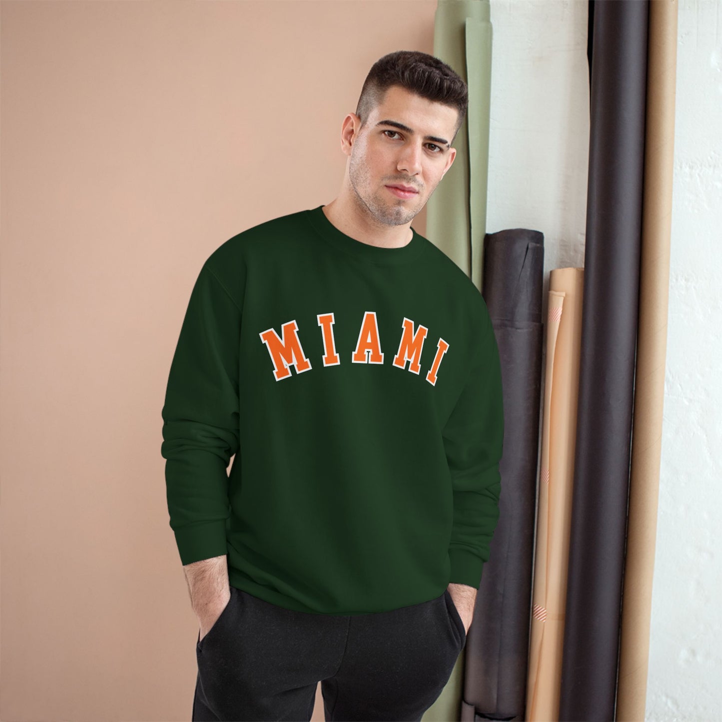 Man wearing a green sweatshirt with 'MIAMI' printed on it, standing against a beige wall.