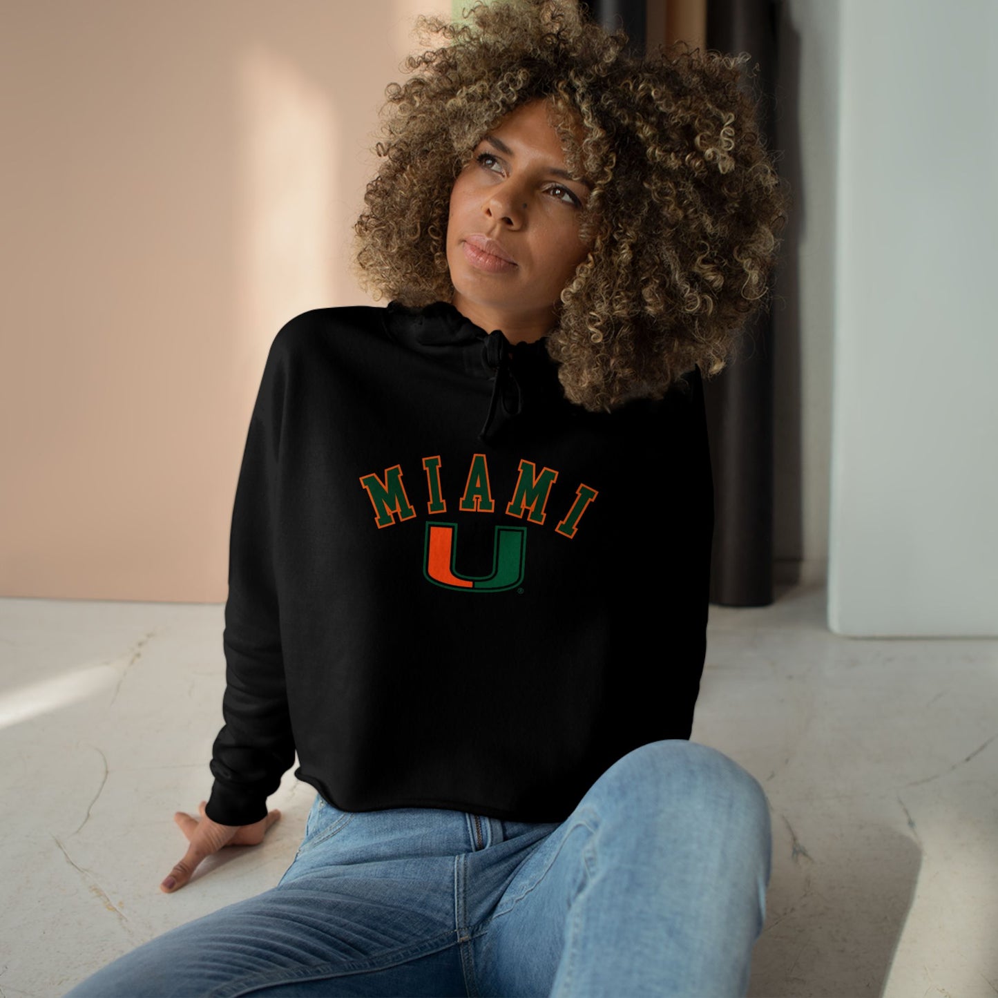 Person wearing a black hoodie with 'MIAMI U' text sitting on the floor.