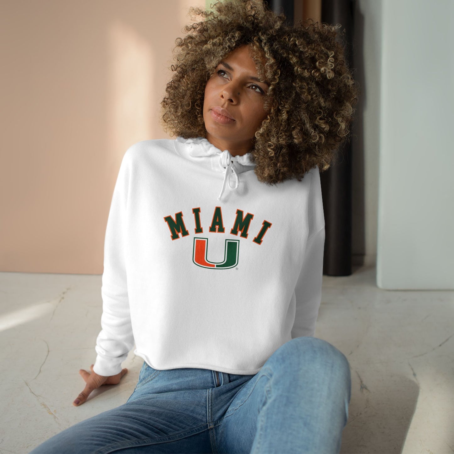 Woman wearing a white hoodie with 'MIAMI U' text, sitting indoors.