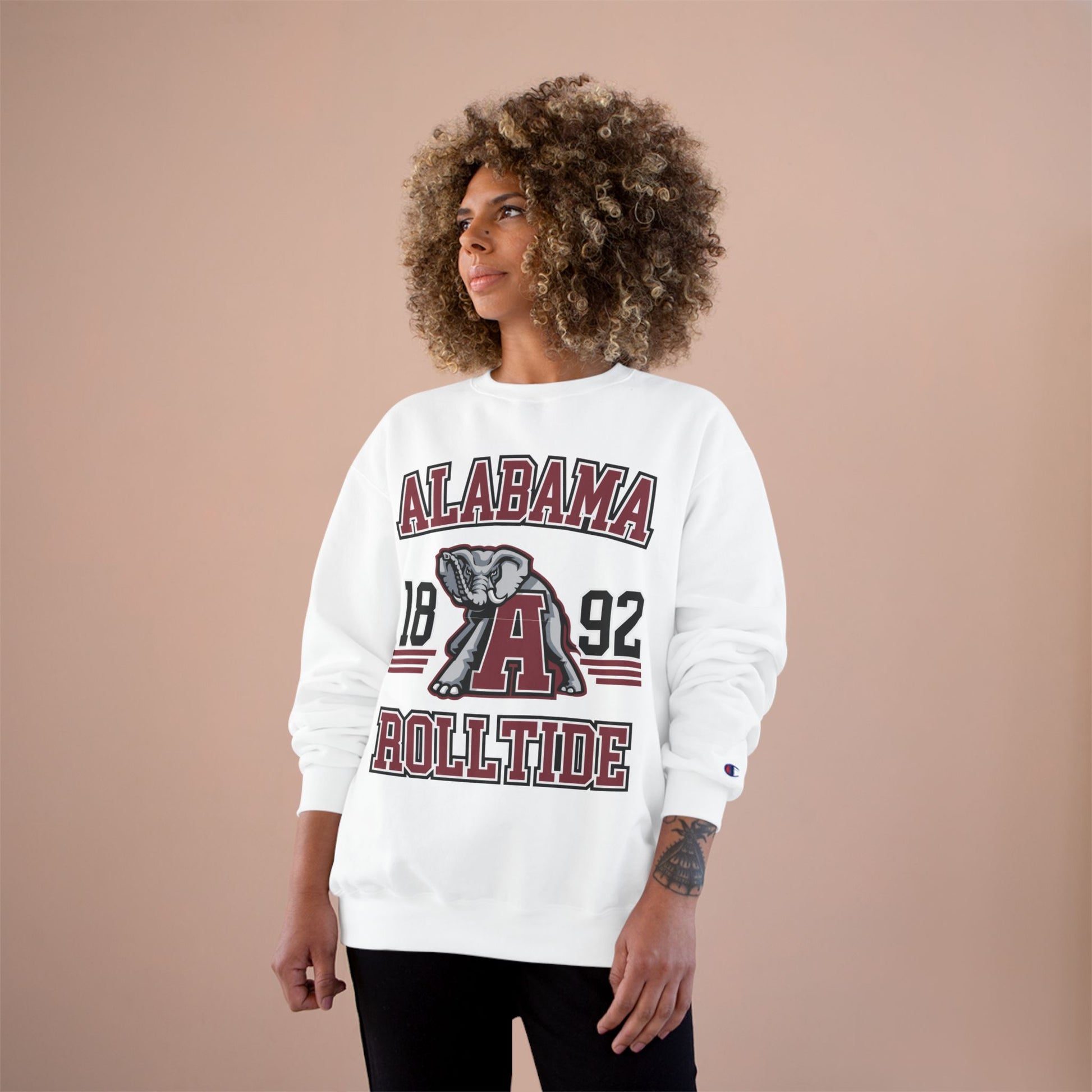 Person wearing a white 'Alabama Roll Tide' sweatshirt with an elephant graphic on a beige background