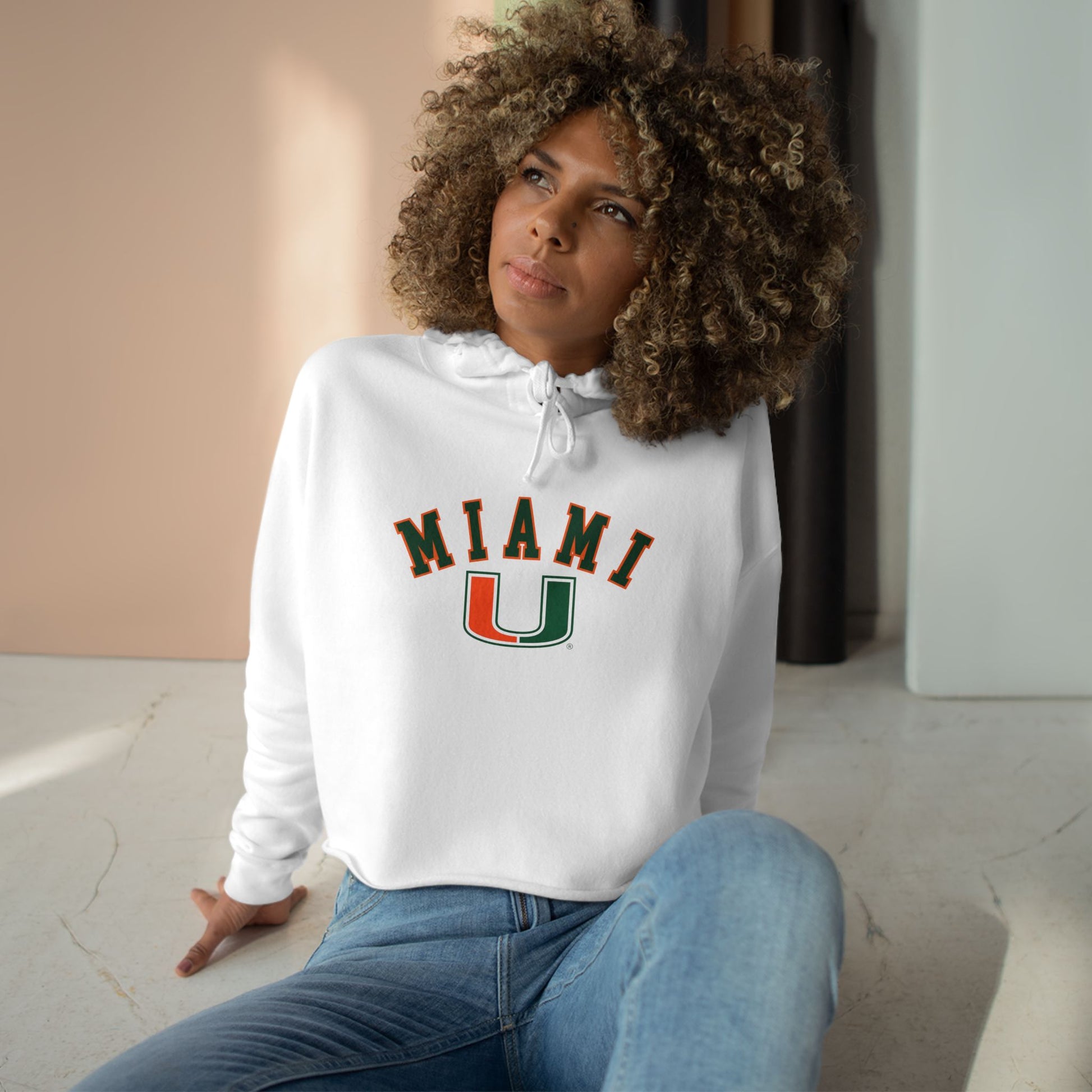 Woman wearing a white hoodie with 'MIAMI U' text, sitting indoors.